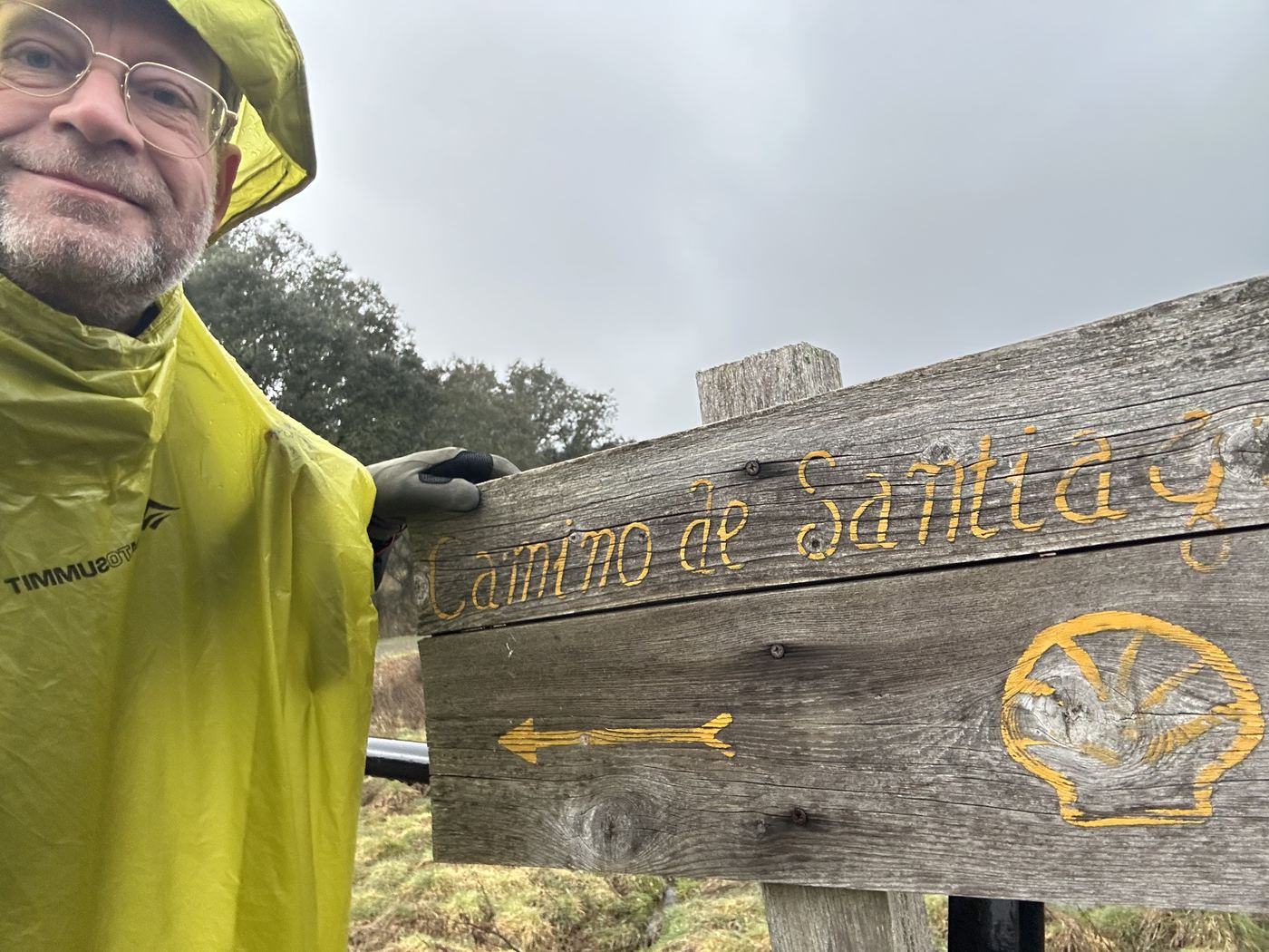 Edwin in gele poncho bij Camino-bord, in de regen